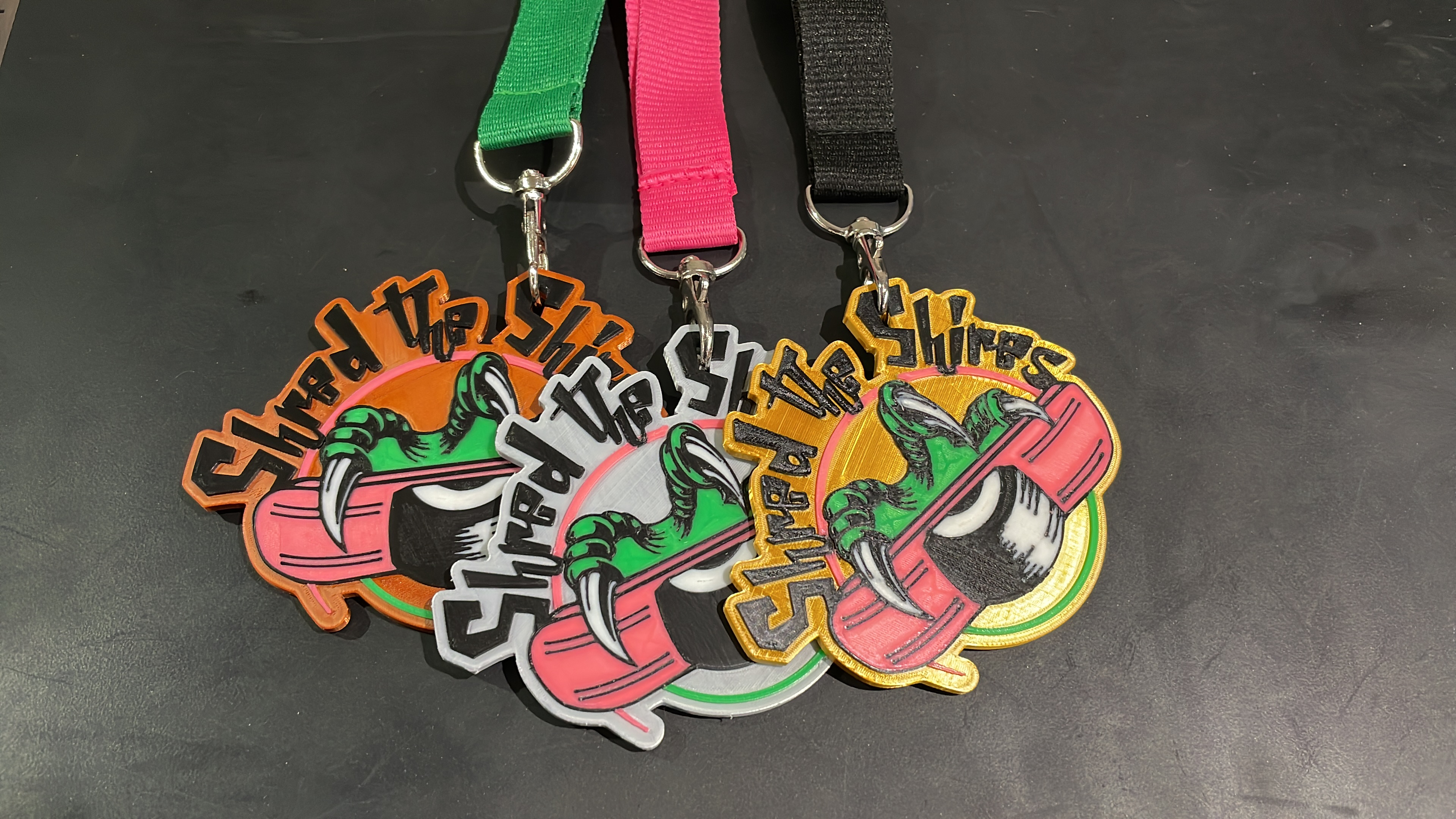 Three multi-colour Shred the Shires medals on green, pink and black lanyards